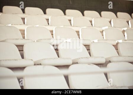 Simili vecchi sedili bianchi vuoti in cemento con schienale arrotondato messo in file su livelli diversi vicino muro di mattoni in abbandonato stadio Foto Stock