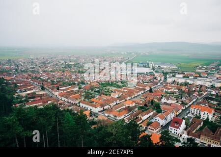 Da sopra vista panoramica della piccola città di San Giorgio in Transilvania con cottage accoglienti e circondato da verdi colline Foto Stock