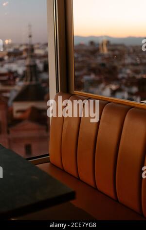 Comodo divano in pelle nella moderna caffetteria situata sulla terrazza sul tetto Con parete di vetro con vista sulla città di Madrid durante il tramonto ora Foto Stock