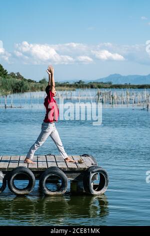 Corpo pieno di un ragazzo tranquillo barefooted in esecuzione di abbigliamento casual Signore della posa di yoga di Dance e mudra di Gyan sul molo di legname in giornata di sole Foto Stock