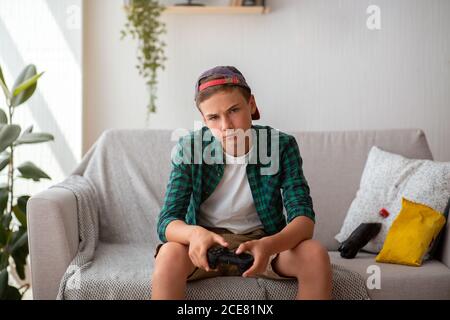 Ragazzo teenager annoiato che tiene il joystick, seduto sul divano Foto Stock