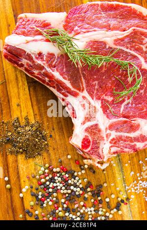 Carne di manzo cruda sul tavolo, spezie e rosmarino, costolette ingredienti. Pepe e sale grosso Foto Stock