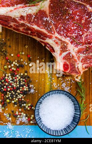 Carne di manzo cruda sul tavolo, spezie e rosmarino, costolette ingredienti. Pepe e sale grosso Foto Stock