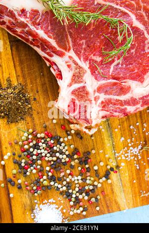 Carne di manzo cruda sul tavolo, spezie e rosmarino, costolette ingredienti. Pepe e sale grosso Foto Stock