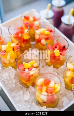 Alto angolo di bicchieri con fresca Macedonia di frutta fatta con frutta colorata assortita servita su vassoio con ghiaccio Foto Stock