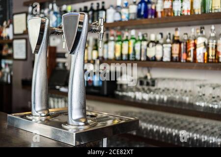 Colonna di birra metallica posizionata sul banco bar contro i ripiani con bevande alcoliche in bottiglie di vetro Foto Stock