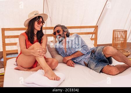 Coppia matura felice a lunghezza intera in un abbigliamento casual estivo seduto sul letto in campeggio di lusso e guardando ciascuno altro con tenerezza Foto Stock