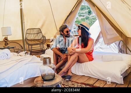 Coppia matura felice a lunghezza intera in un abbigliamento casual estivo seduto sul letto in campeggio di lusso e guardando ciascuno altro con tenerezza Foto Stock