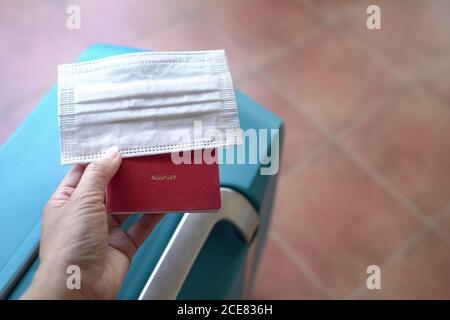 Donna che tiene maschera e passaporto con valigia sullo sfondo. Viaggio durante la pandemia del coronavirus. Foto Stock