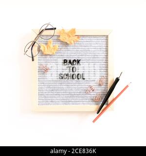 Citazione Torna a scuola. Composizione autunnale con cartoncino, bicchieri, cancelleria, foglie di acero essiccate su sfondo bianco Foto Stock