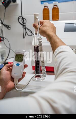 Coltivare anonimo scienziato maschile conducendo la ricerca in laboratorio con la misurazione dispositivo e provetta con soluzione rossa Foto Stock