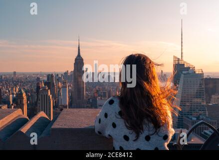 Vista posteriore di una donna anonima in piedi sul punto di vista di Alto edificio e osservando il paesaggio urbano di New York City durante tramonto Foto Stock