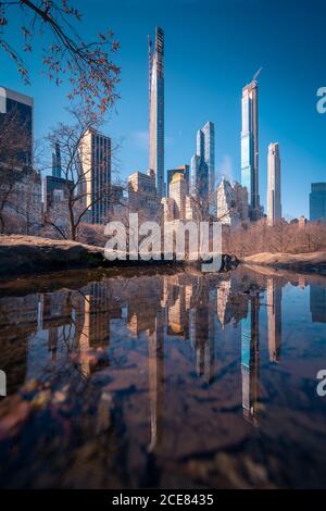 Basso angolo di moderne torri cittadine situate vicino a Central Park con alberi senza foglie contro il cielo blu in sole primavera giorno A New York Foto Stock