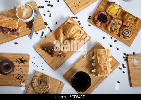 Vista dall'alto sul tavolo della colazione, ricco di pasticcini assortiti, panini e caffè serviti su tavole di legno Foto Stock