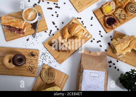 Vista dall'alto sul tavolo della colazione, ricco di pasticcini assortiti, panini e caffè serviti su tavole di legno Foto Stock