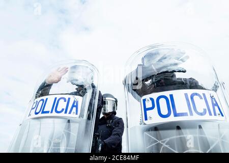 Basso angolo di soldati di polizia anonimi in uniformi protettive e. caschi in piedi contro furgone di squadra e difendendo da scudi di rivolta Foto Stock