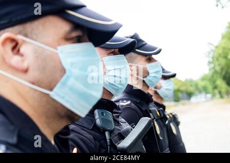 Squadra a corpo pieno di poliziotti spagnoli in attrezzi protettivi con pistole che indossano maschere mediche durante la pattugliatura della strada Foto Stock