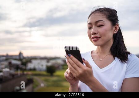 Donna che seleziona l'uomo mentre riposa sulla terrazza e sta navigando datando app sullo smartphone Foto Stock
