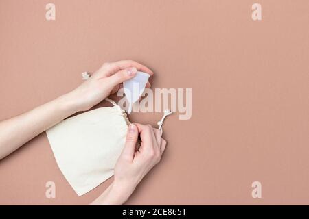 Le mani femminili prendono la tazza mestruale dalla borsa di tela. Concetto di zero sprechi su sfondo marrone con spazio di copia. Foto Stock
