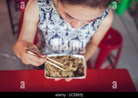 Dall'alto di una femmina etnica troncata e irriconoscibile seduta al bancone Nel mercato notturno di Zhubei e mangiare riso a base di olio glutinoso con bastoncini di pollo Foto Stock