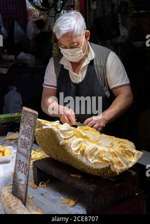 Hong Kong, Cina:12 Mar, 2020. Un uomo taglia Jackfruit fino a vendere sul mercato in Canton Road Mong Kok.Alamy Stock Image/Jayne Russell Foto Stock