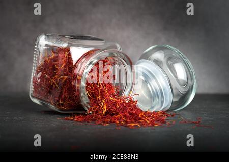 Zafferano aromatico essiccato spruzzato dal vaso di vetro sul tavolo sfondo grigio in studio Foto Stock