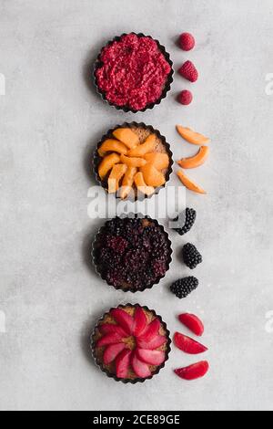 Vista dall'alto di torte gustose con vari frutti maturi e. bacche disposte in linea sul tavolo Foto Stock