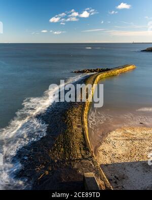 Le onde rompono sulla pietra della parete del porto di Baia Cullercoats Tyneside sulla costa del Mare del Nord. Foto Stock