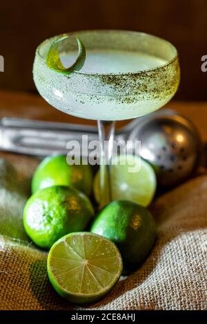 Bicchiere di mojito fresco e mazzo di lime mature messe su sackcloth ruvido sul tavolo Foto Stock