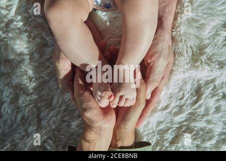 Le mani della madre tengono i piedi del bambino su un tappeto bianco Foto Stock