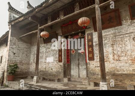 Esterno di un vecchio edificio in pietra con pareti in shabby e ornamentale Porta con lanterne di carta nella contea di Yangshuo Foto Stock