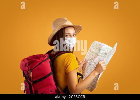 Ragazza gioiosa con zaino grande che tiene la mappa, indossando maschera protettiva Foto Stock