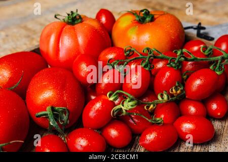 Vista dall'alto di vari tipi di pomodori rossi maturi freschi su vassoio di legno disposto su rustico tavolo di legno con stoffa Foto Stock