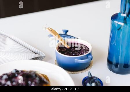 Da sopra deliziosi pancake fatti in casa con marmellata di mirtilli serviti con tazza di caffè, frutti di bosco freschi e banana sul tavolo impostazione per il brunch in casa in una cucina accogliente Foto Stock