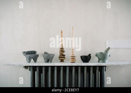 Vari utensili da cucina, tra cui mortai con pestelli disposti in fila sul banco in marmo vicino al muro Foto Stock