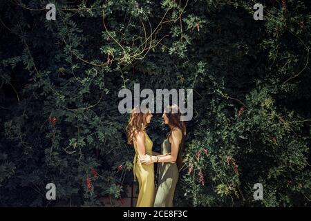 Vista laterale di affascinante giovane figlia e snella mezza età madre che si guarda l'un l'altro e abbracciando teneramente in verde giardino in estate Foto Stock