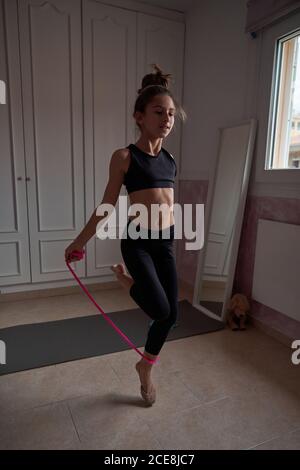 Corpo pieno di teen slender ginnast in nero sport salto corda mentre si allenano nella propria stanza a casa guardando via Foto Stock