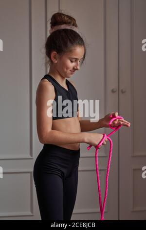 Teen ginnasta snella in nero sportswear che si prepara per la corda di salto mentre si allenano nella propria stanza a casa guardando via Foto Stock