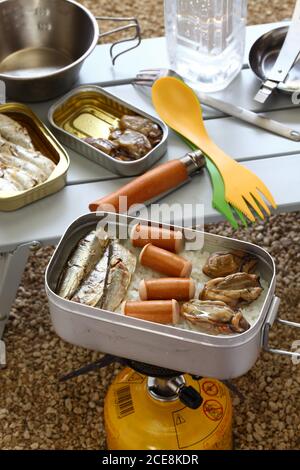 cucina da campeggio. sardine oliate, salsicce e ostriche affumicate su riso bollito in scatola di pasticcio. Foto Stock