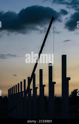 silhouette di cantiere con gru e colonne al tramonto Foto Stock