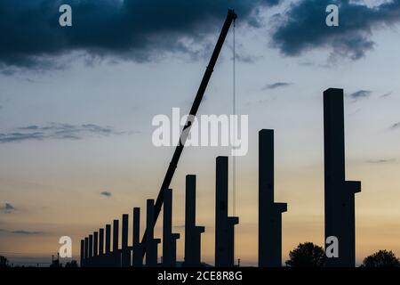silhouette di cantiere con gru e colonne al tramonto Foto Stock