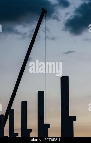 silhouette di cantiere con gru e colonne al tramonto Foto Stock