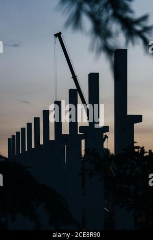 silhouette di cantiere con gru e colonne al tramonto Foto Stock