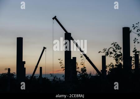 silhouette di cantiere con gru e colonne al tramonto Foto Stock