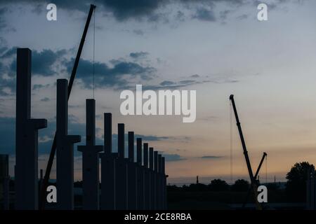 silhouette di cantiere con gru e colonne al tramonto Foto Stock