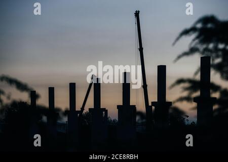 silhouette di cantiere con gru e colonne al tramonto Foto Stock