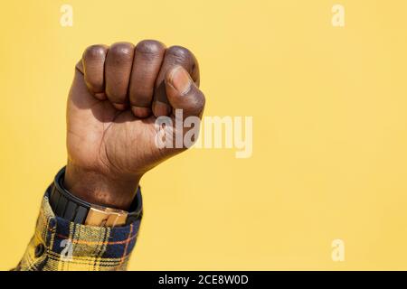 il pugno sollevato di un uomo nero su uno sfondo giallo intenso, il concetto di lotta per i diritti umani e lo stile di vita, spazio di copia per il testo Foto Stock