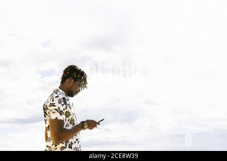 elegante giovane uomo nero che guarda il suo cellulare con il cielo in background, tecnologia e stile di vita concetto, copia spazio per tex Foto Stock