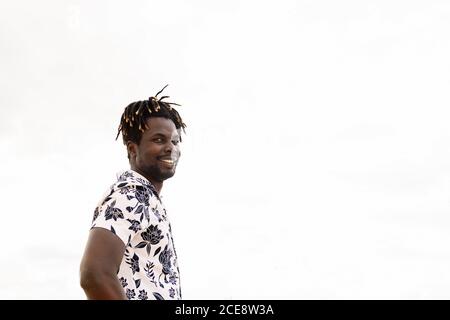 elegante giovane uomo nero con camicia di fiori e cielo sullo sfondo sorridente sulla fotocamera, concetto di libertà e stile di vita, spazio di copia per il testo Foto Stock