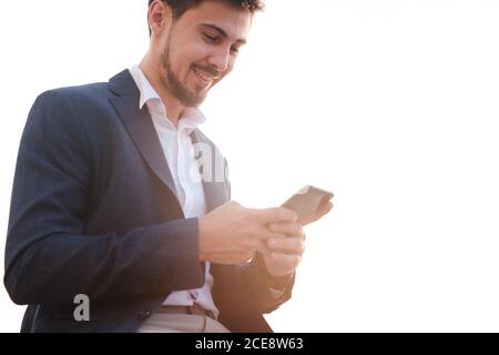 Sotto la vista di sorridente bearded manager in giacca utilizzando il cellulare internet al telefono all'aperto Foto Stock